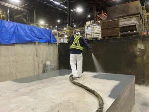worker spraying waterproof resinous coating over primary containment system in a warehouse industrial facility